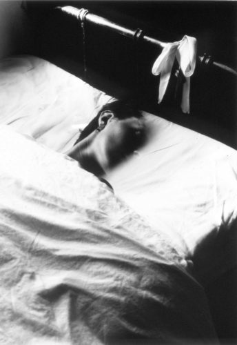 woman under white blanket in bed with her face partly vanishing into the background, b/w